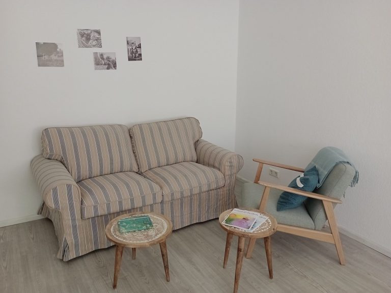 Sitzecke in der Naturheilpraxis Binoth mit Sofa, Sessel und kleinen Tischchen.